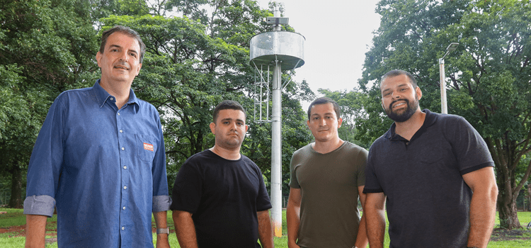 Equipe da Neger Telecom formada por quatro homens brancos posam para a foto em área verde e arborizada, com a torre de monitoramento ao fundo. Fim da descrição.