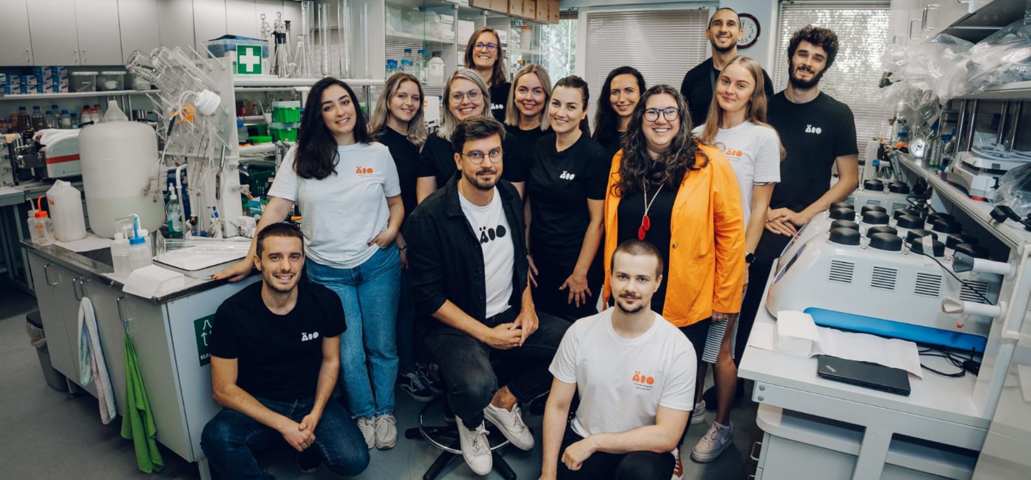 Equipe da ÄIO, composta por nove mulheres e cinco homens, dentro de laboratório da empresa. Fim da descrição