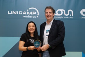 Andrea Matsui com o troféu em nome da Generation Brasil, empresa-filha da Unicamp vencedora do Prêmio Empreendedor da Unicamp 2024 na categoria Impacto Socioambiental & Diversidade. Ao seu lado está Eduardo Neger, da Neger Telecom. Fim da descrição.