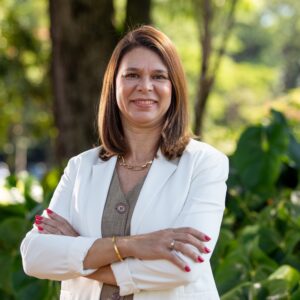 Mariana Zanatta Inglez, coordenadora de ambientes de inovação e empreendedorismo da Inova Unicamp, posa com os braços cruzados, sorrindo para a câmera, em um ambiente externo com folhagens verdes ao fundo. Ela veste um blazer branco sobre uma blusa marrom.Mariana Zanatta Inglez, coordenadora de ambientes de inovação e empreendedorismo da Inova Unicamp, posa com os braços cruzados, sorrindo para a câmera, em um ambiente externo com folhagens verdes ao fundo. Ela veste um blazer branco sobre uma blusa marrom. Fim da descrição.