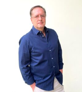 Waldemar Felippe, presidente-executivo do conselho do Unicamp Ventures, em uma foto de estúdio, olhando diretamente para a câmera, com as mãos nos bolsos. Ele usa uma camisa social azul escura e calças claras, em fundo branco. Fim da descrição.