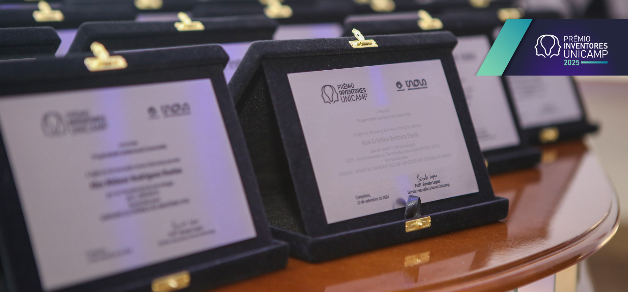 Vista parcial de uma mesa de premiação com vários prêmios em estojos pretos. É possível ler "PRÊMIO INVENTORES UNICAMP 2025" no canto superior direito. Fim da descrição.